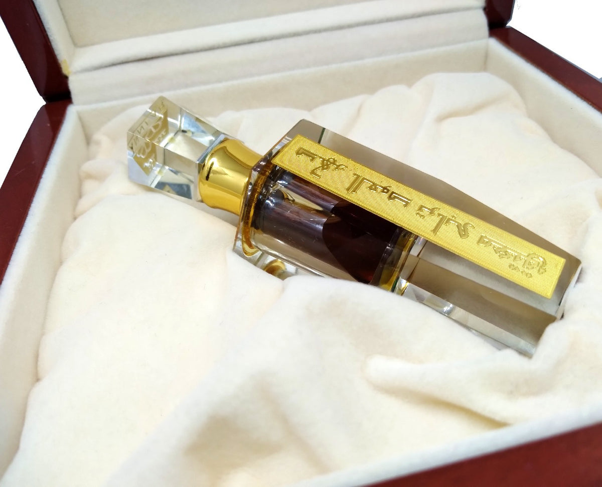 Ornate glass bottle with dark oil and a gold Arabic label, nestled in a plush-lined wooden presentation box.