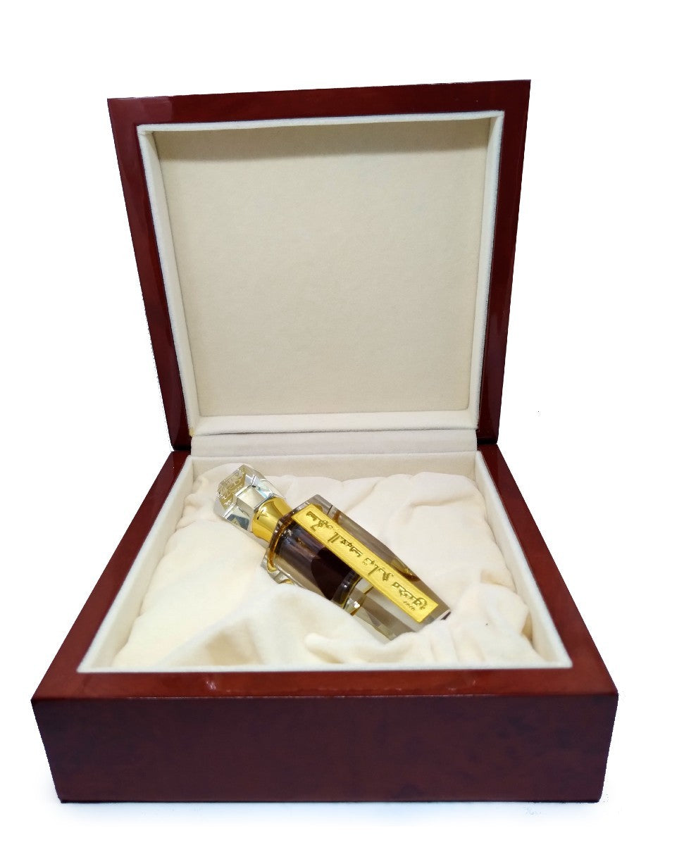 Small glass perfume bottle with gold label and dark liquid inside an open, plush-lined dark wood box.