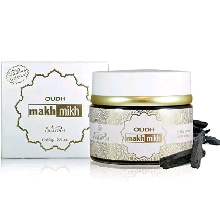 Nabeel Oudh Makh Mikh cosmetic jar with its white packaging box and a few dark dried flower buds on a white background.