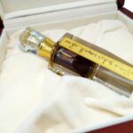 Ornate glass bottle with dark oil and a gold Arabic label, nestled in a plush-lined wooden presentation box.