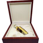 Small glass perfume bottle with gold label and dark liquid inside an open, plush-lined dark wood box.